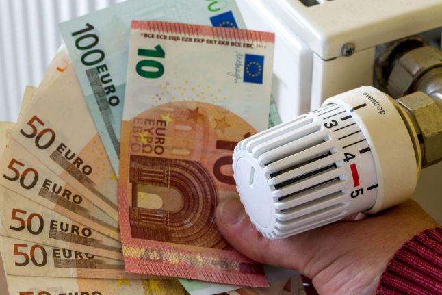 A man holds a wad of euro notes next to a radiator.