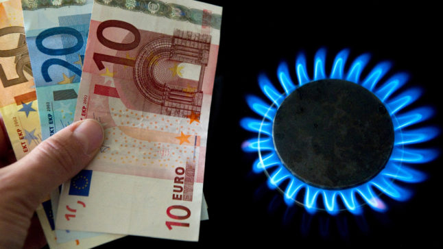 A woman holds euro bills next to a gas flame on a kitchen stove in Frankfurt (Oder).