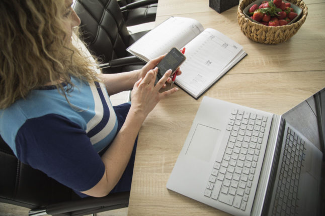 A woman in Germany uses a phone and laptop. Germany is working on a digital strategy.