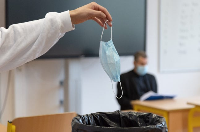 A school pupil places a disposable mask in the bin