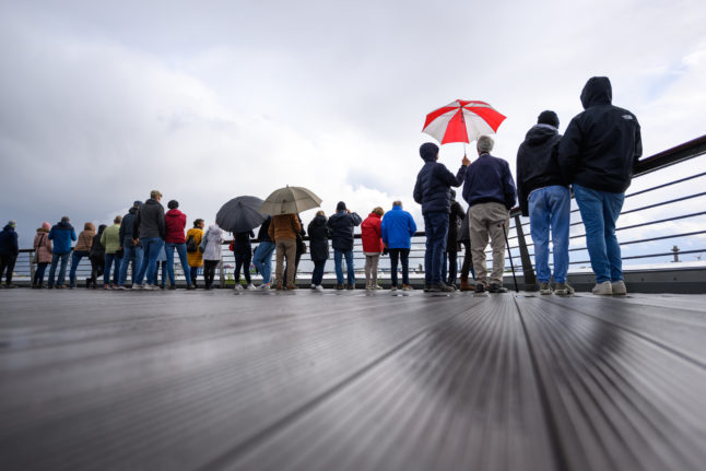 People stand with umbrellas under grey clouds at the Hamburg Cruise Centre Altona