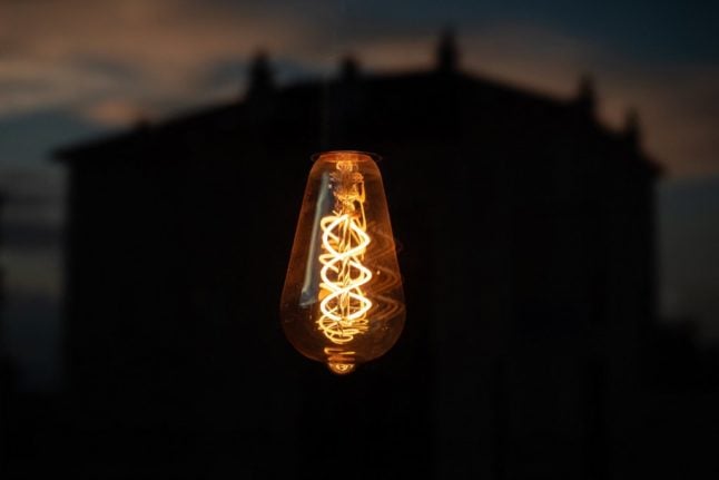 A picture taken on August 28, 2022 shows an incandescent light bulb with a residential building seen in reflection on a window after sunset in Lausanne.