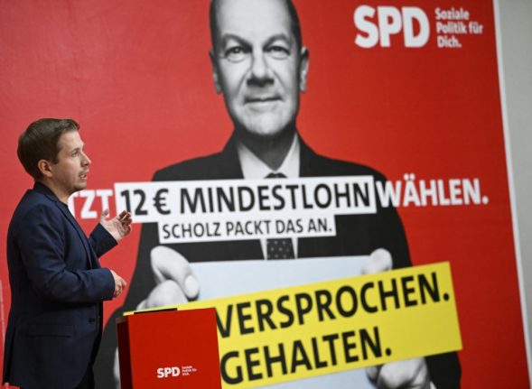 Social Democratic Party General Secretary Kevin Kuehnert addresses a press conference in front of a placard showing German Chancellor Olaf Scholz and the words 'Now vote for 12 Euro minimum wage - promise kept' 