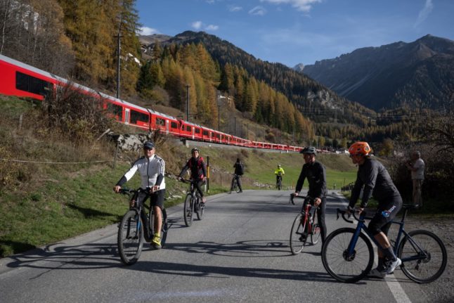 Cyclists watch as a 1910-metre-long train with 100 cars passes near Bergun, on October 29, 2022, during a record attempt by the Rhaetian Railway (RhB) of the World's longest passenger train, to mark the Swiss railway operator's 175th anniversary. 