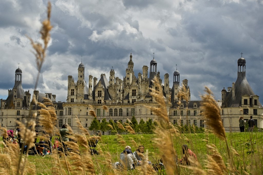 People sit on the grass in front of the castle of Chambord