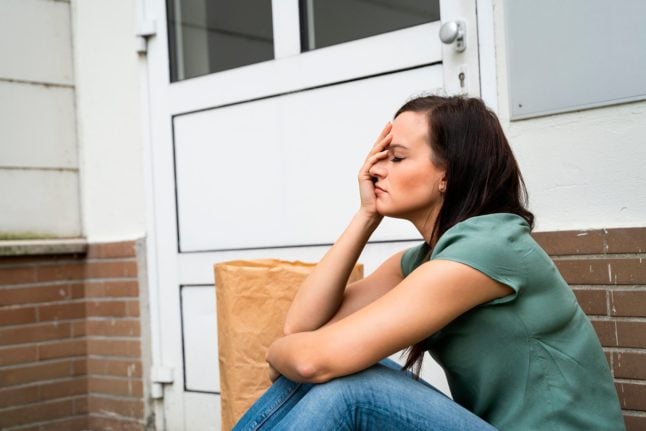 A woman sits outside her front door having locked herself out of her home.