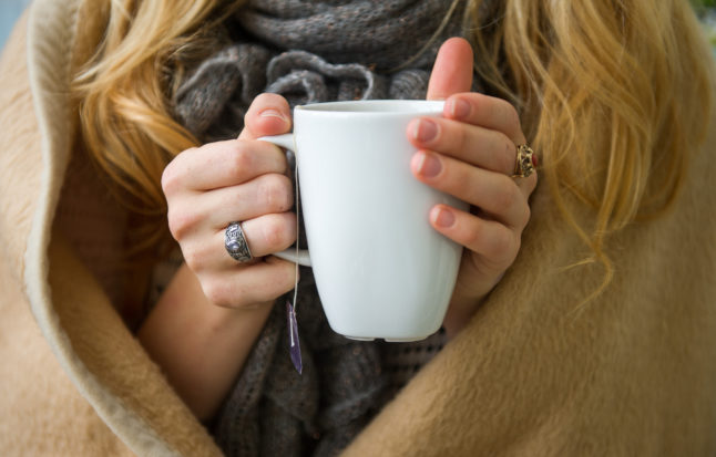 A woman warms up with tea and a blanket in a German flat.