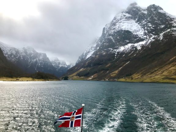 Pictured is a Norwegian flag with a fjord backdrop.