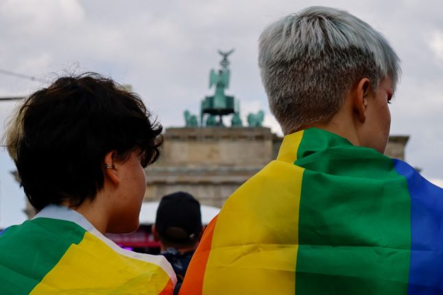 People draped in rainbow flags take part in the Christopher Street Day demonstration in memory of the Stonewall Riots during Pride month with Berlin's Brandenburg Gate in the background.