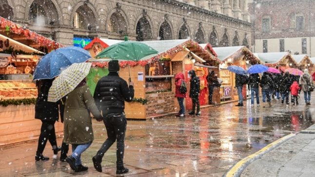 People walk across a Christmas market in downtown Milan as snow falls on December 8, 2021.