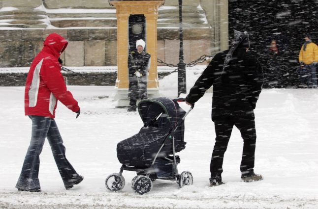 Tourists walk past a soldier of The Royal Guard outside the castel in Stockholm during a heavy snowstorm.