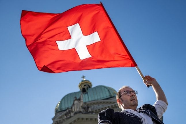 A flag thrower performs with a Swiss flag in front of the Parliament.
