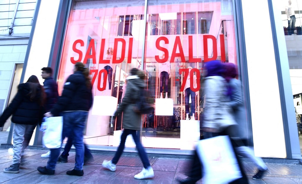 People walk past a clothing store announcing sales in Milan on January 5, 2018.