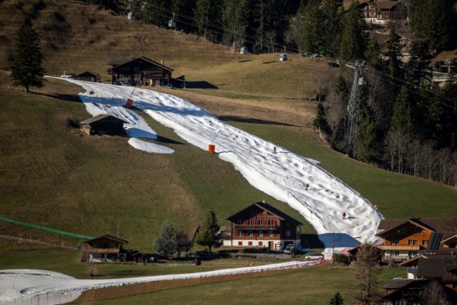 Skiers slide down a slope where snow remains at Adelboden Swiss alpine resort
