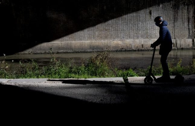 A man rides an e-scooter along the River Tiber bike path.