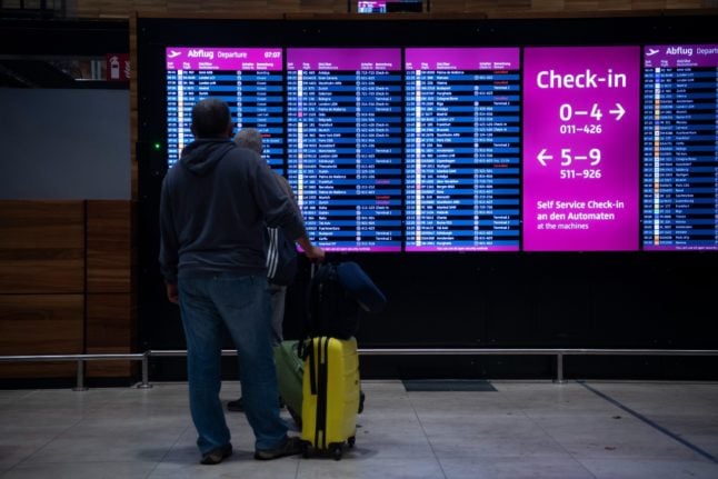Two travellers are standing in front of an information board at BER Airport.