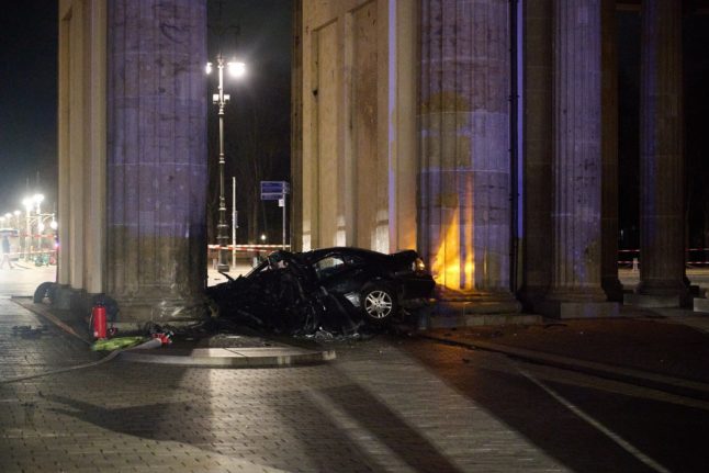A wrecked car lies in front of a pillar of the Brandenburg Gate.