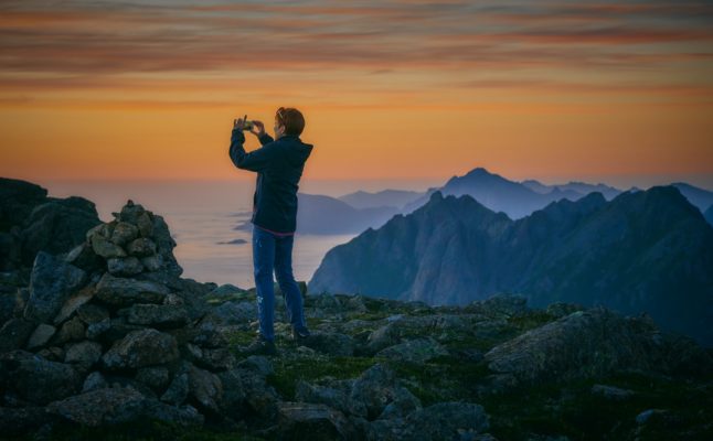Pictured is a person watching a sunset atop a mountain.