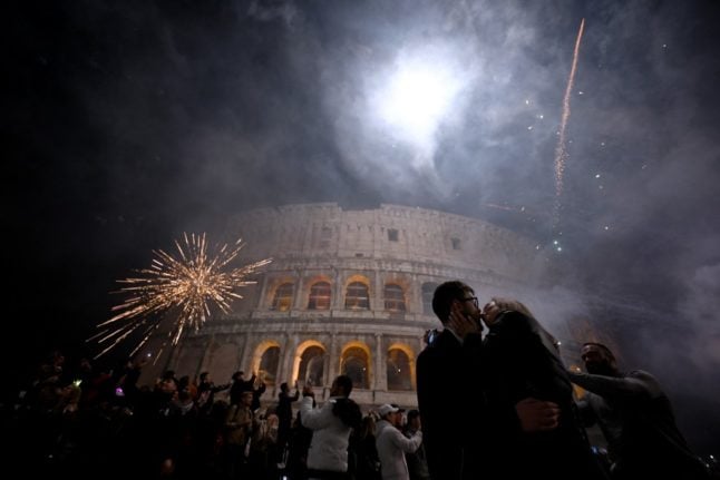 A couple kisses as fireworks are shot as part of celebrations for the New Year in downtown Rome, with the ancient Colosseum in the background, on January 1, 2023. 