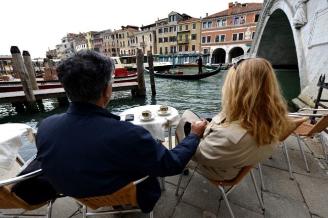 A couple take a coffee in a bar next to the Rialto bridge in downtown Venice on April 26, 2021. - Bars, restaurants, cinemas and concert halls will partially reopen across Italy on April 26 in a boost for coronavirus-hit businesses, as parliament debates the government's 220-billion-euro ($266-billion) EU-funded recovery plan. After months of stop-start restrictions imposed to manage its second and third waves of Covid-19, Italy hopes this latest easing will mark the start of something like a normal summer.