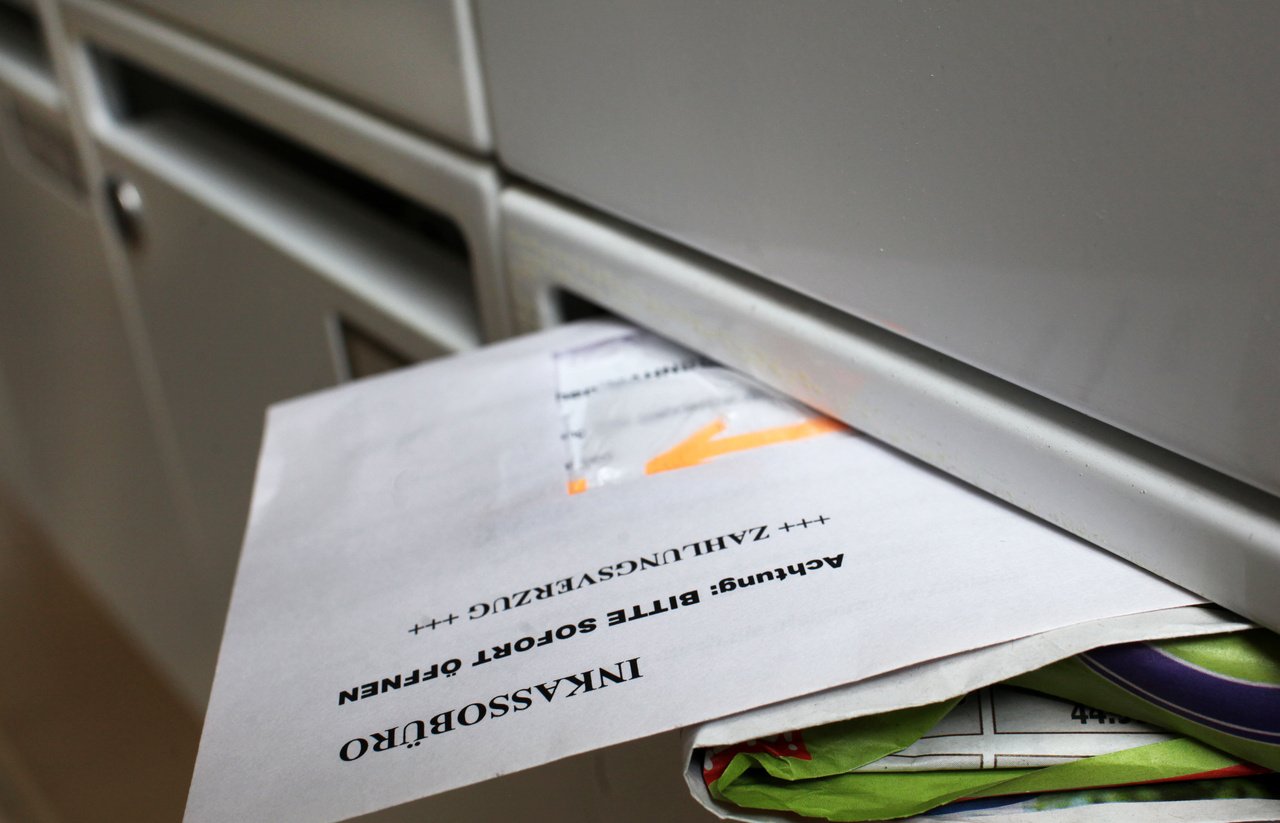 A letter from a debt collection agency sticks out of a post box.