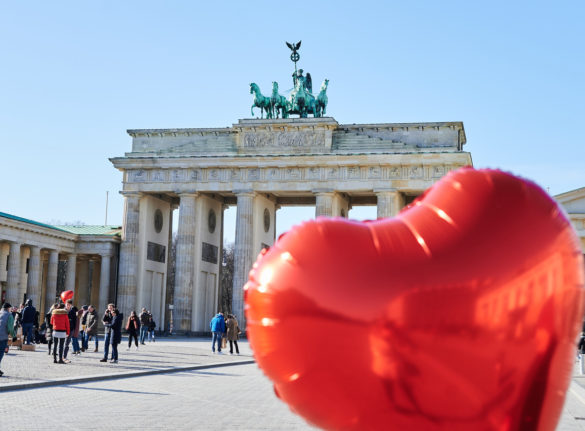 A woman holds a heart-shaped balloon in front of the Brandenburg Gate in Berlin.