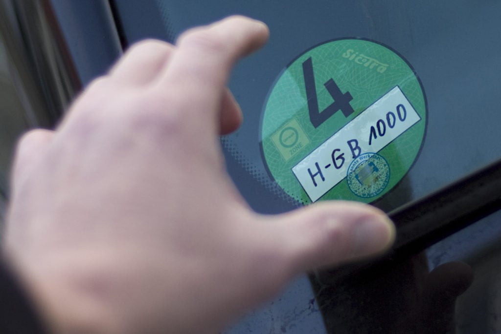 A hand reaches for a green environmental badge on a car in Hanover.