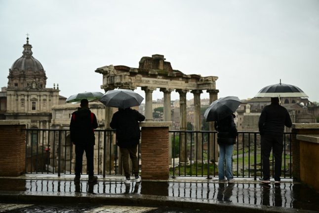 Tourists holding umbrellas as rain pours in Italy