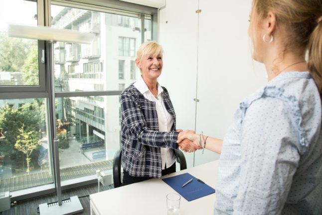 A hiring manager and applicant shake hands at a job interview.