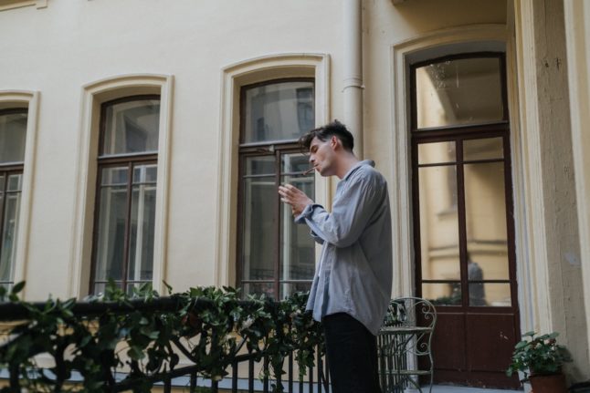 A man spokes a cigarette on a residential balcony.