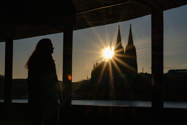 A woman observes the sun setting behind Cologne Cathedral.