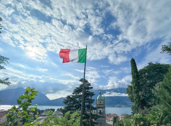 An Italian flag waves in the wind, with Lake Como in the background