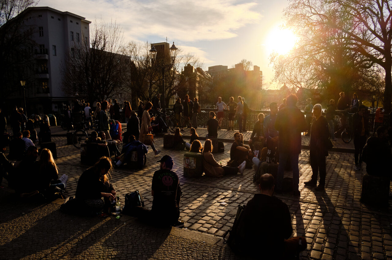 Numerous people sit in the light of the setting sun on the Admiralbrücke in Berlin's Kreuzberg district.