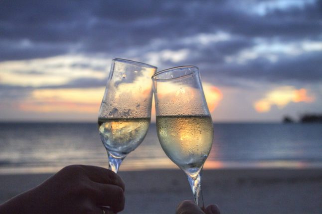 Two people toast with champagne on a beach.