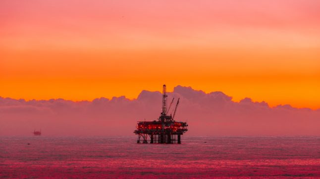 Pictured is stock photo of an oil rig at sunset.