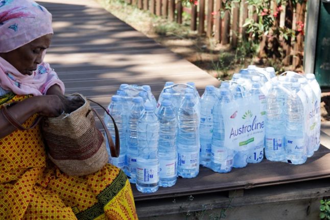 A Mayotte resident sits with packs of water she has received at a distribution point as she awaits a lift home following the arrival of a ship carrying bottled water for the most vulnerable people on the French island of Mayotte