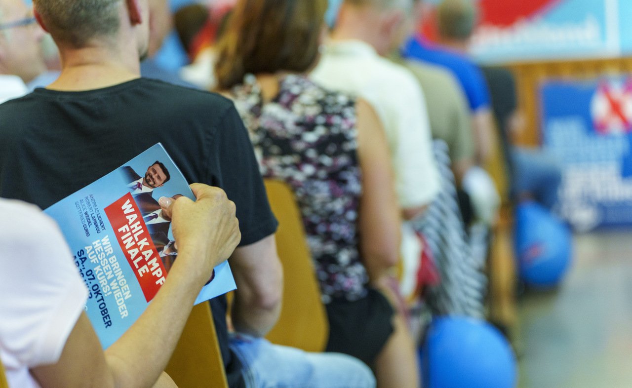 An AfD supporter holds a "campaign finale" leaflet that shows the portraits of the top Hessian AfD candidates for the state election.