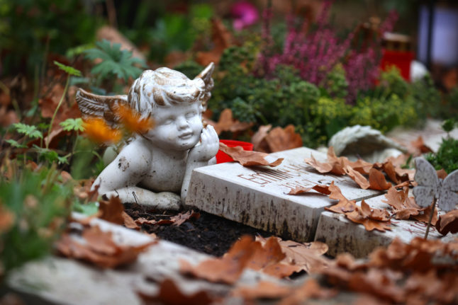 An angel figure lies on a grave among autumn leaves at the Central Cemetery in Kempten, Bavaria.