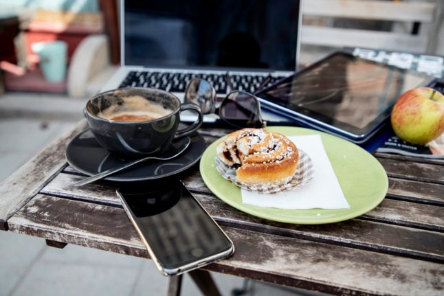 a cinnamon bun on a table with a computer, phone, coffee and ipad