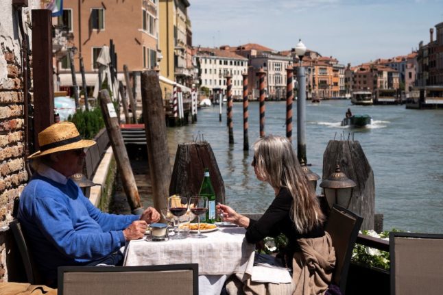Diners sit at the at an outdoor table by the Grand Canal in Venice.