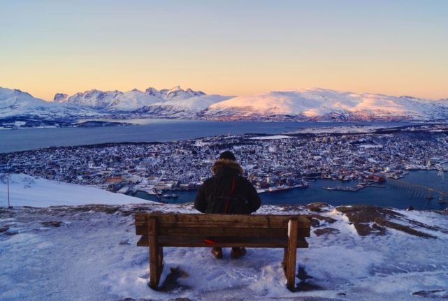 Pictured is a man sat on a bench at a mountain viewpoint overlooking Tromsø.