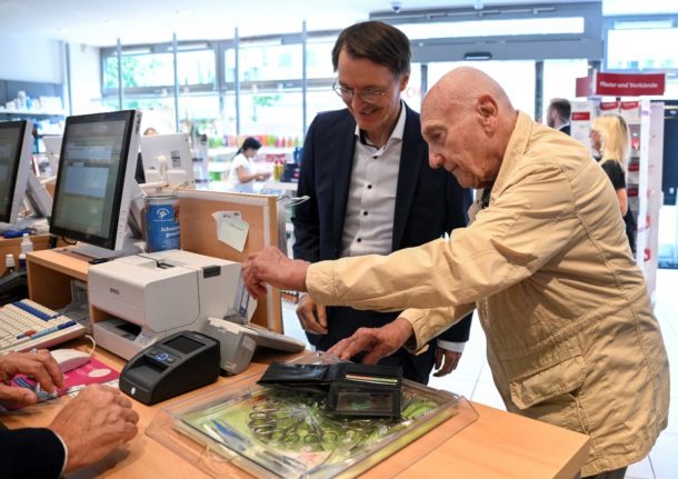 An 86-year-old Berlin resident inserting his health insurance card into a reader to get a prescription alongside German Health Minister Karl Lauterbach.