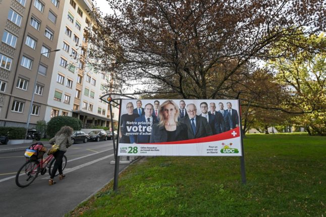 A picture taken on October 17, 2023, shows a cyclist pushing her bike past an electoral poster of candidates of the Swiss People's Party (SVP UDC) in Aarberg ahead of the 2023 Swiss federal elections.