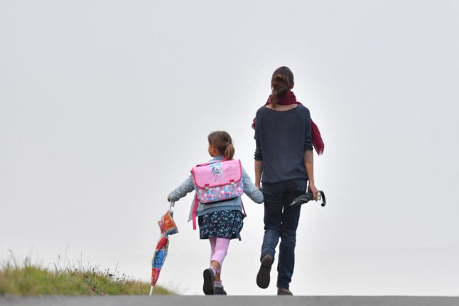 Image from behind of a mother and daughter, who is carrying an umbrella, walking to school
