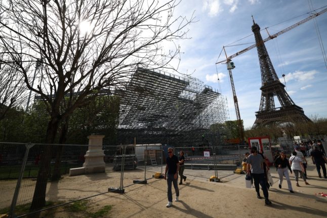 Pedestrians walk past closed-off construction works with the Eiffel Tower in the background at the Champ-de-Mars that will host the beach volleyball competition event during the upcoming Paris 2024 Olympic