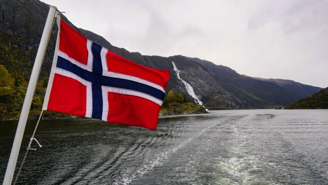 Pictured is the Norwegian flag overlooking a fjord.
