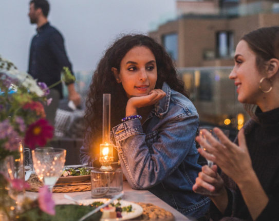two women talking to each other at an outdoor table on a summer evening