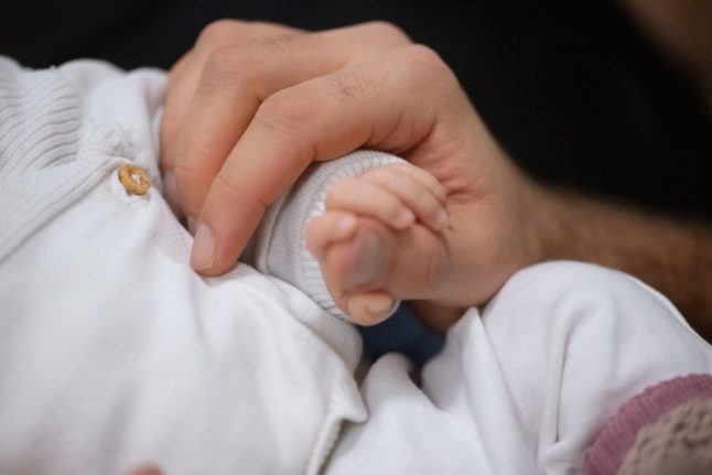 A father in Stuttgart holds the hand of his newborn baby.
