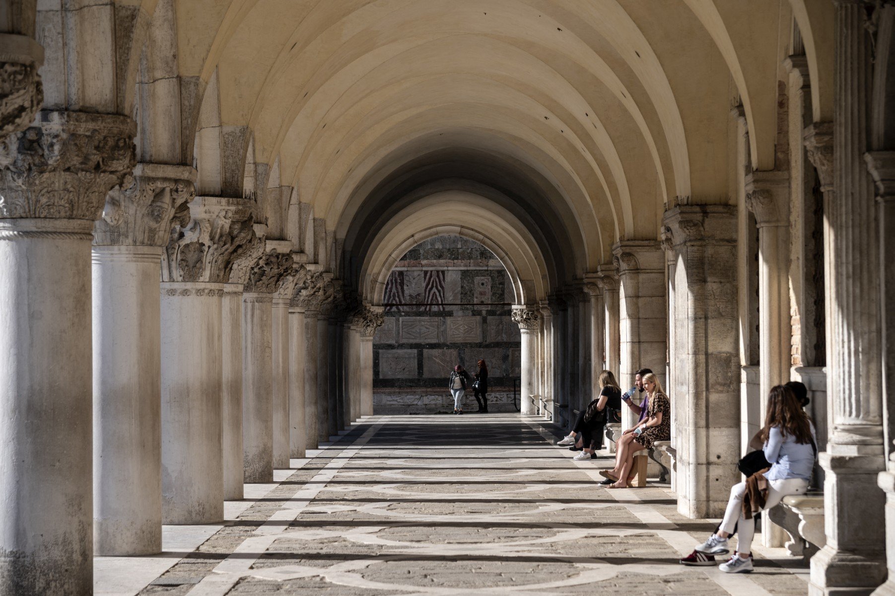 Tourists sit under the archway of the Doge's Palace in Venice