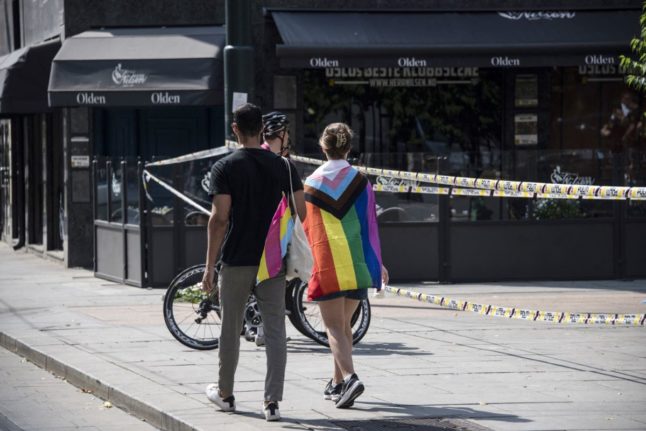 Pictured are two people near the scene of the Oslo shooting wearing progress flags.